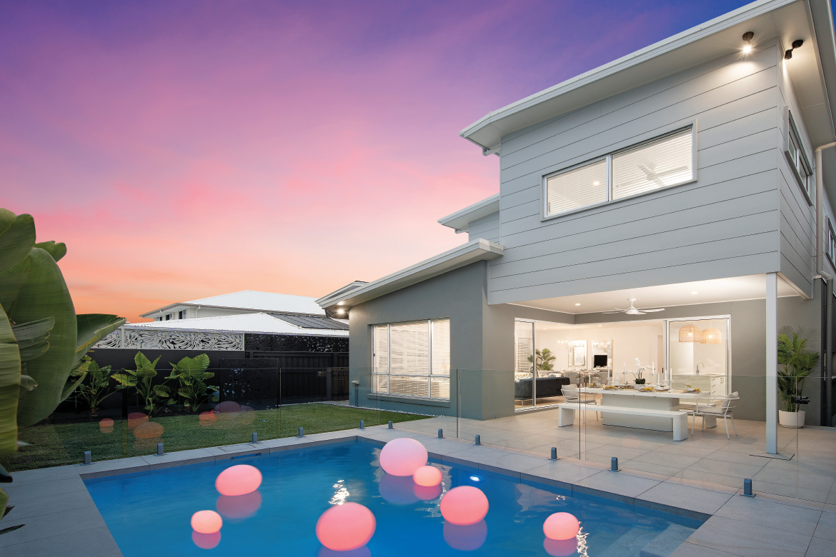 A photo of a modern home with a swimming pool in the yard, taken at dusk
