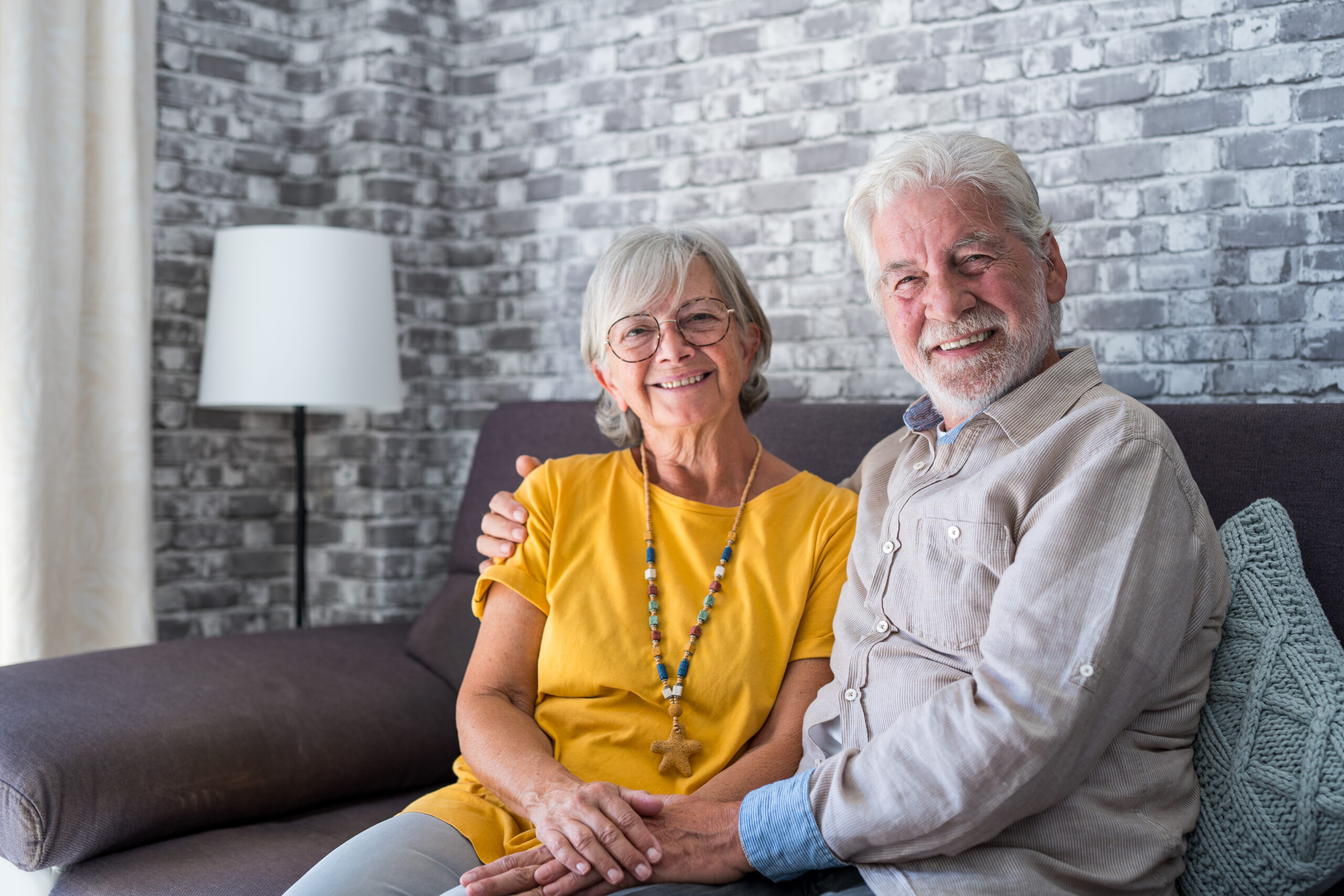 Retired couple relaxing together on comfy couch at modern home smiling staring at camera feel carefree.