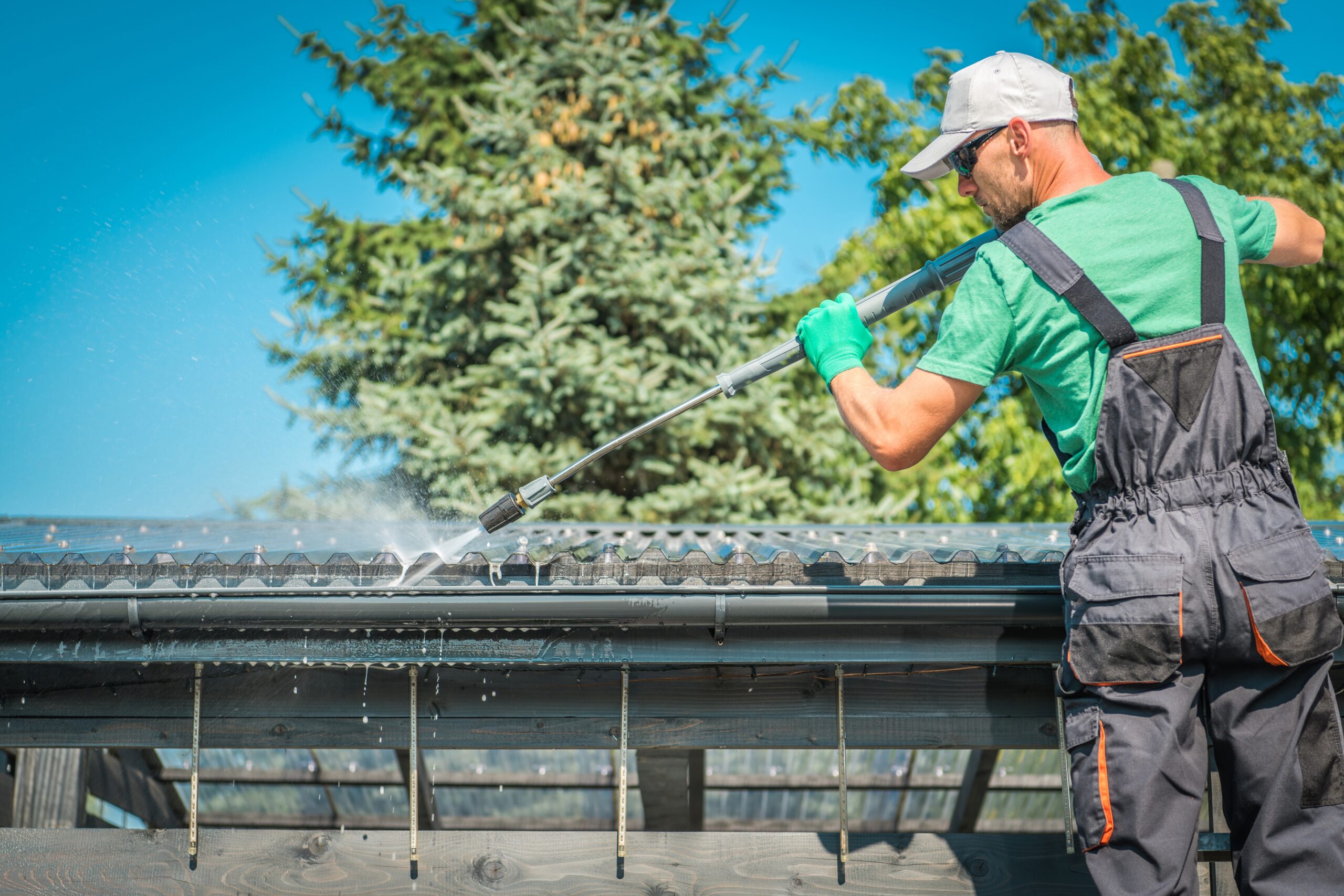 Roof and Gutters Power Cleaning Using Pressure Washer. Caucasian Worker.