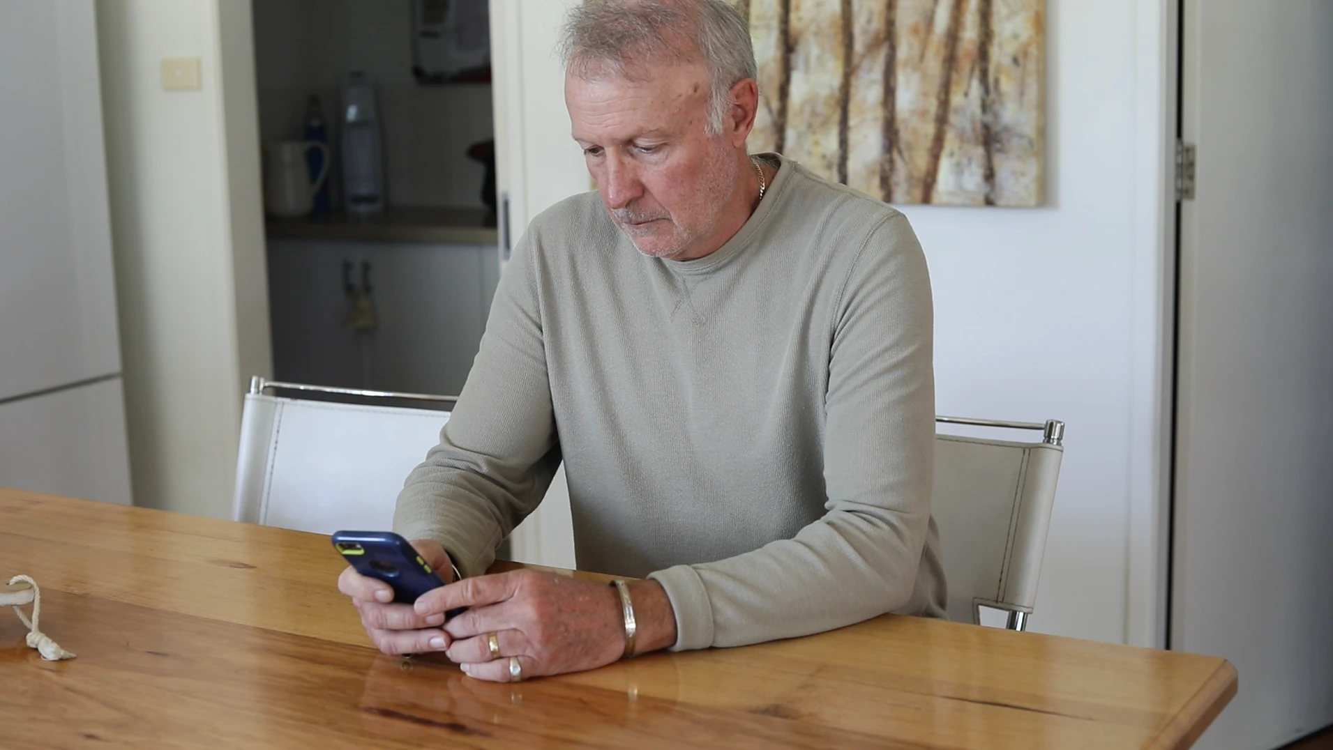 White caucasian man on phone using the MyRedback App in a kitchen with a wooden table.